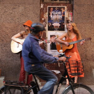 Två kvinnor spelar gitarr på gatan och en man cyklar förbi
